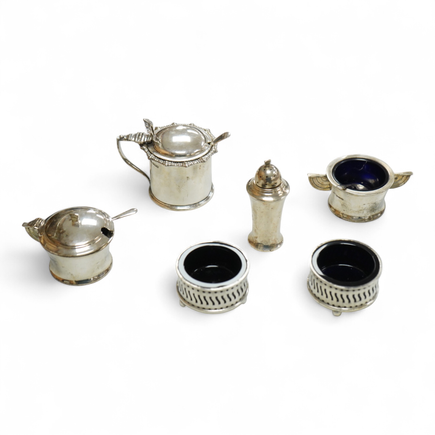 A George V Art Deco three piece silver condiment set and two spoons by William Adams Ltd, Birmingham, 1935, together with a pair of late Victorian pierced silver salts with blue glass liners and an Edwardian silver musta